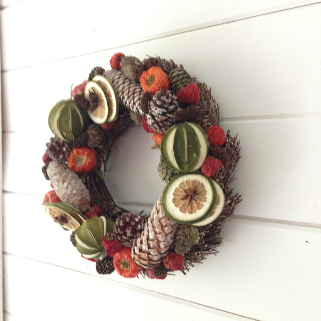 Christmas door wreath decorated with green limes and red peppers, white fir cones on a natural willow base.