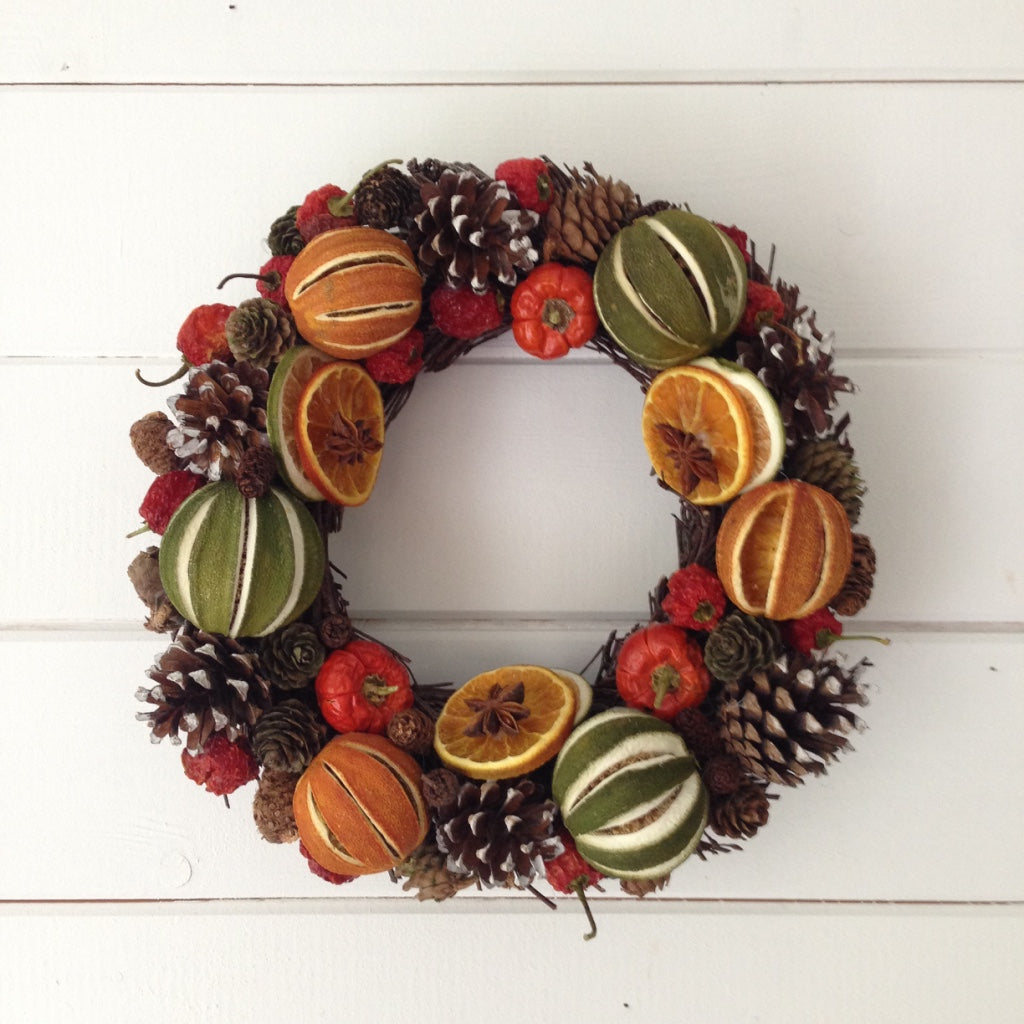 Natural festive green limes oranges, red peppers cones on a natural willow base, creating this Christmas fruit door wreath.