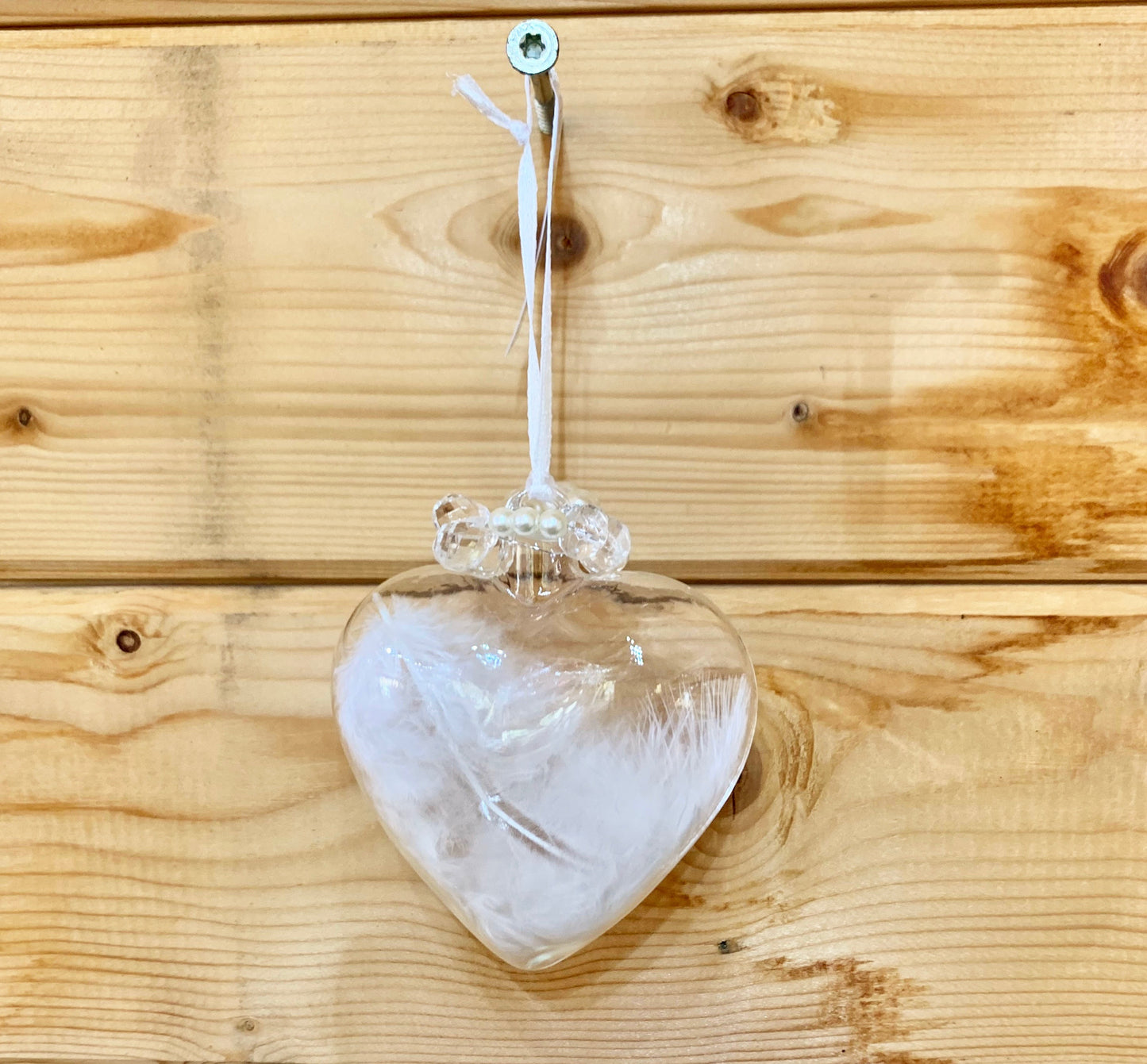 Clear love heart shaped glass hanging Christmas decoration with a white birds feather inside and pearls detail at the top of the heart.