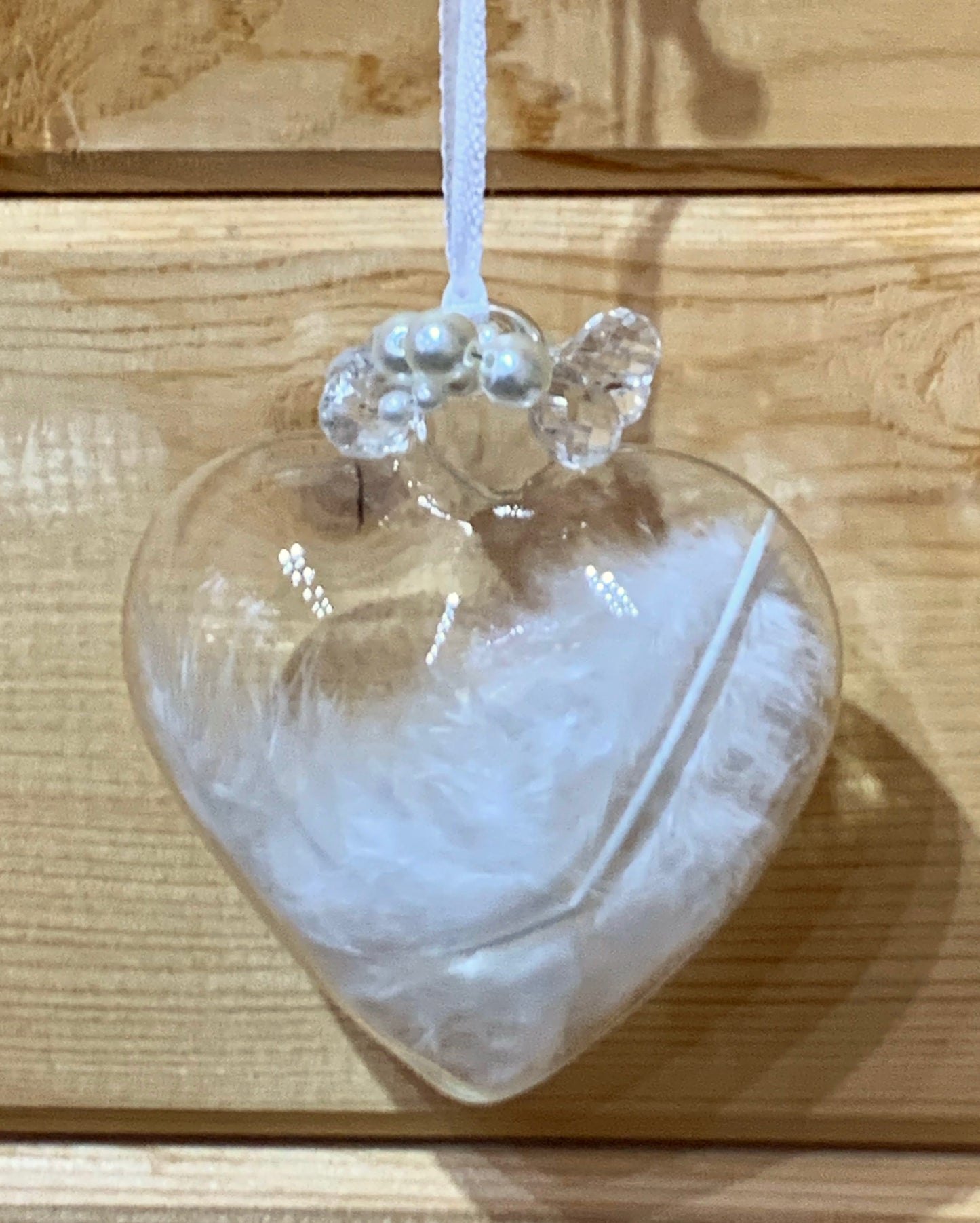 Clear love heart shaped glass hanging Christmas decoration with a white birds feather inside and pearls detail at the top of the heart.