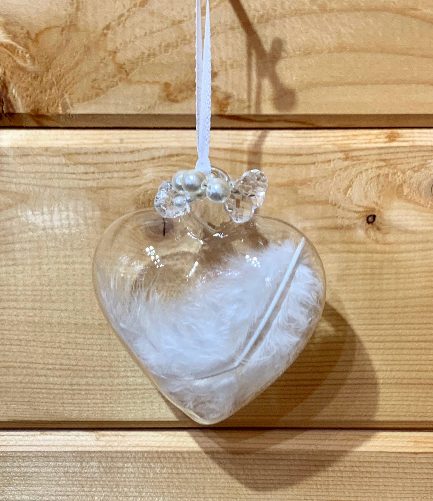 Clear love heart shaped glass hanging Christmas decoration with a white birds feather inside and pearls detail at the top of the heart.