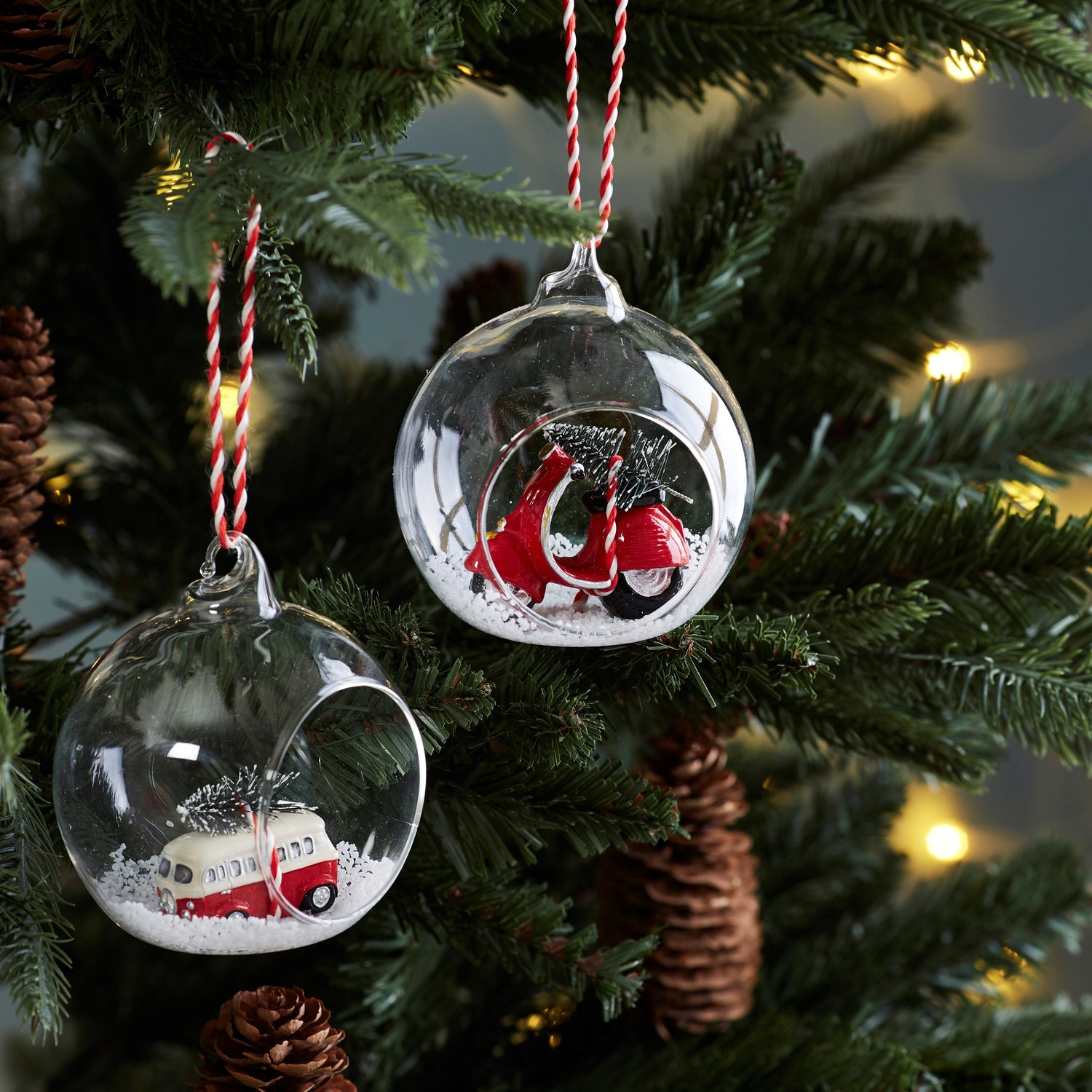 Open glass bauble with a red and white scooter carrying a Christmas tree in the snow.