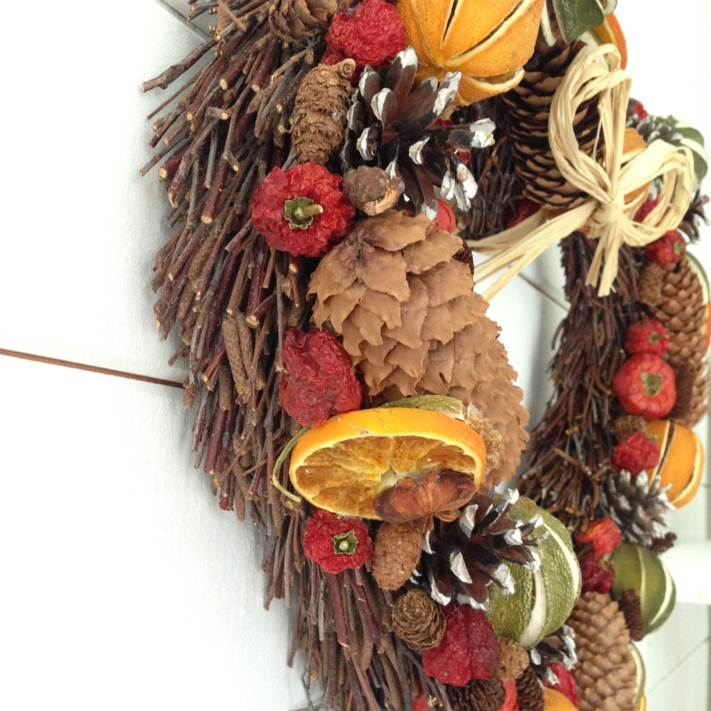 Heart shaped Christmas door wreath decorated with limes oranges and red peppers fir cones on a natural willow heart shaped base.