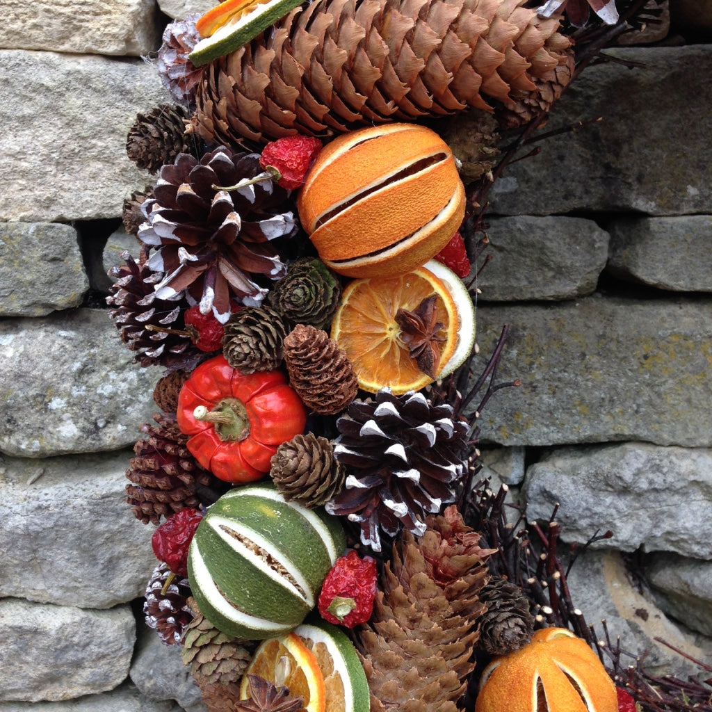Large door Christmas fruit wreath with green limes oranges and red peppers fir cones on a natural willow base 58cms wide.