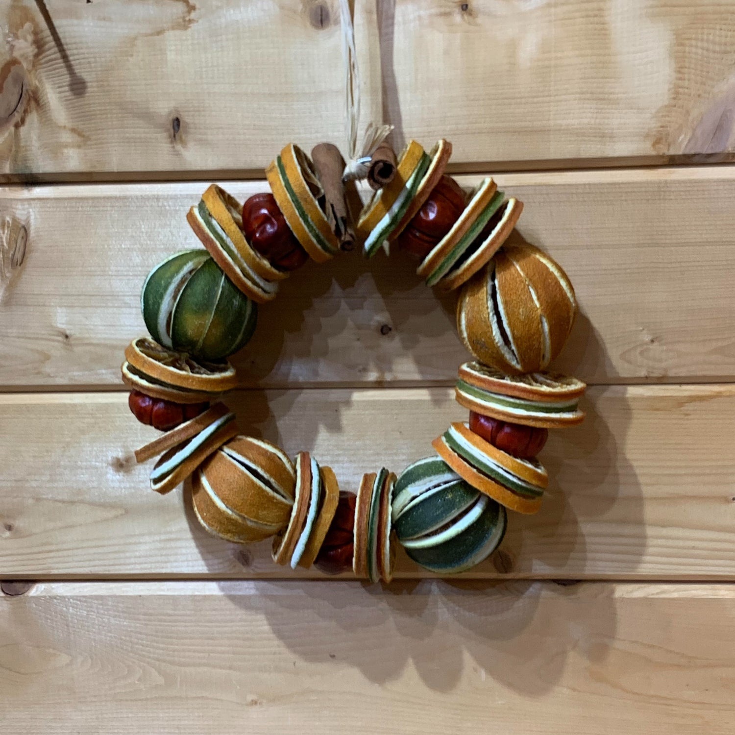A gorgeous Christmas circle shaped wreath for your door made up of dried whole and sliced oranges and limes, small red peppers and cinnamon sticks on a wire base.