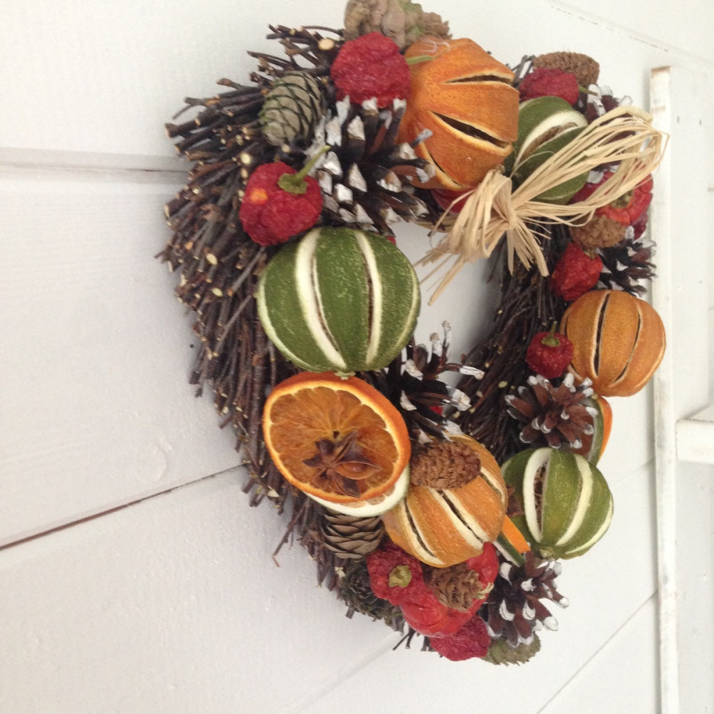 Heart shaped Christmas door wreath decorated with limes oranges and red peppers fir cones on a natural willow heart shaped base.