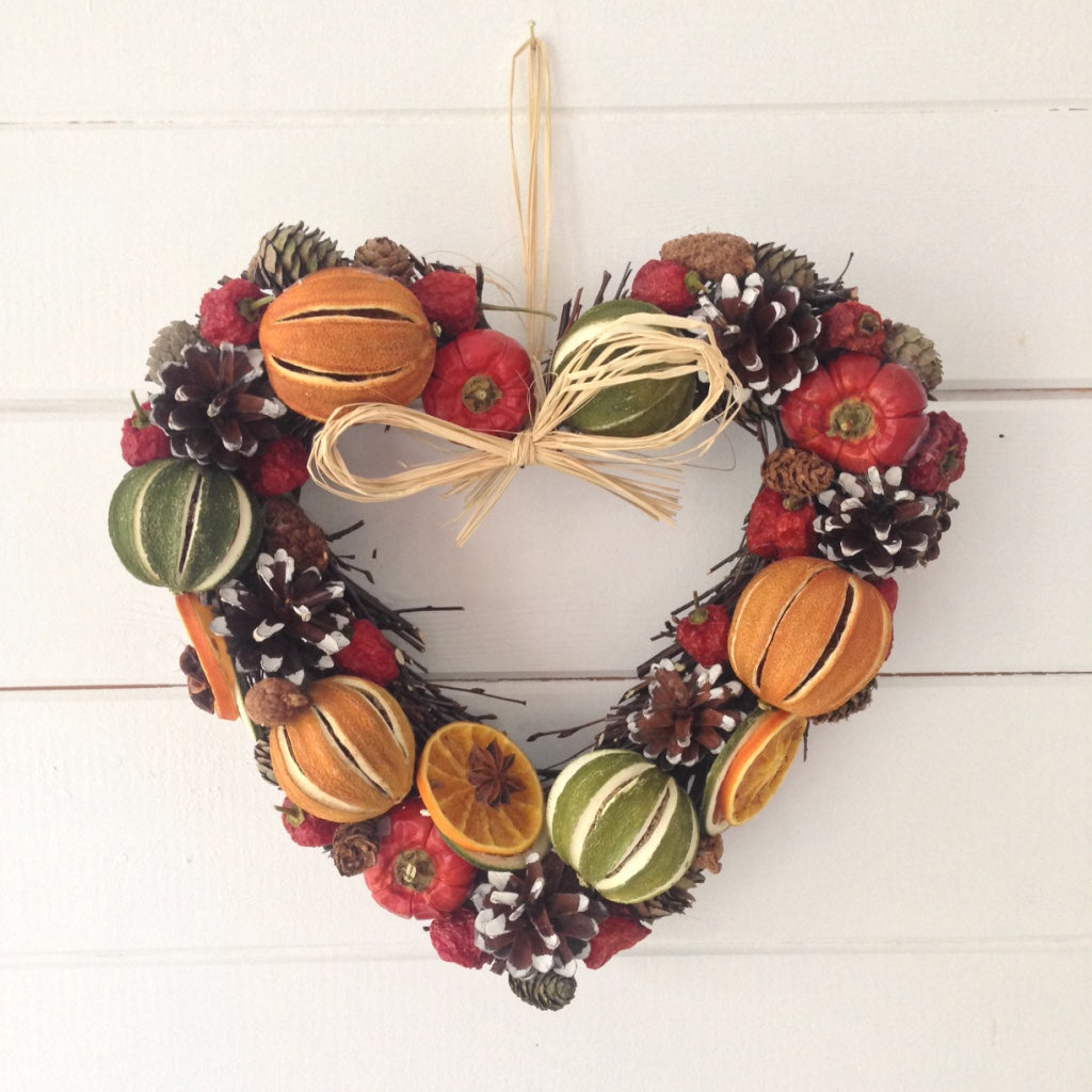 Heart shaped Christmas door wreath decorated with limes oranges and red peppers fir cones on a natural willow heart shaped base.