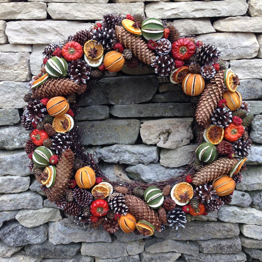 Large door Christmas fruit wreath with green limes oranges and red peppers fir cones on a natural willow base 58cms wide.