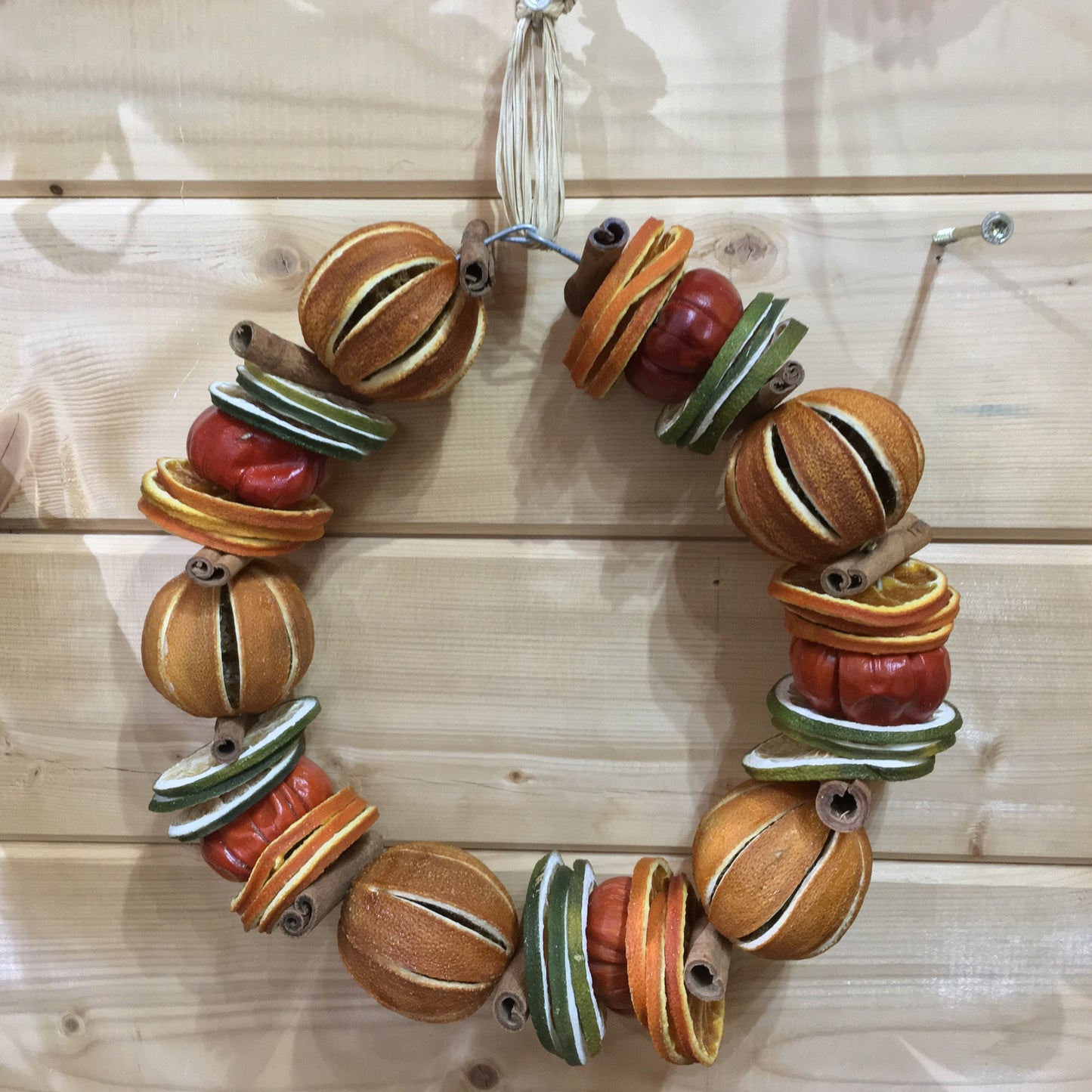 Hanging Christmas fruit circle decoration made from dried whole oranges and sliced limes with cinnamon sticks and small red peppers.