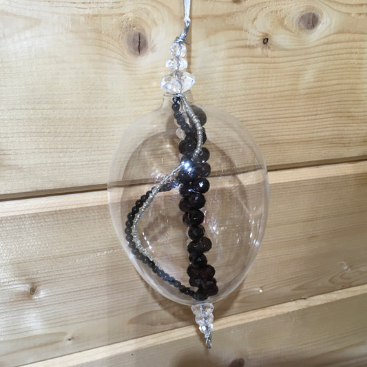 Clear egg-shaped decoration wi8th strings of black, clear and silver beads inside.