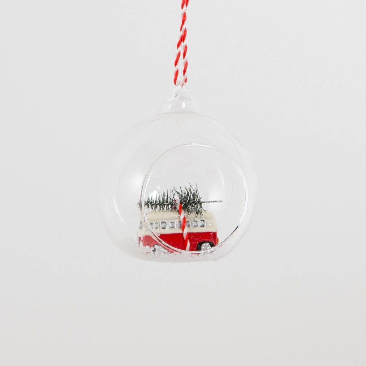 Open glass bauble with a red and white campervan carrying a Christmas tree in the snow.