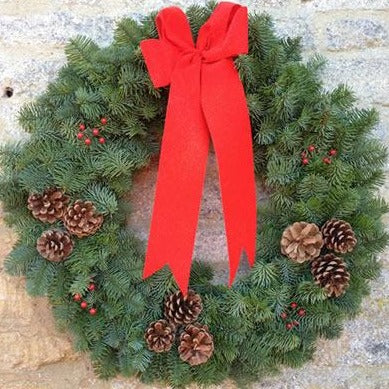 Natural noble fir wreath has been decorated with a large red ribbon and clusters of fir cones