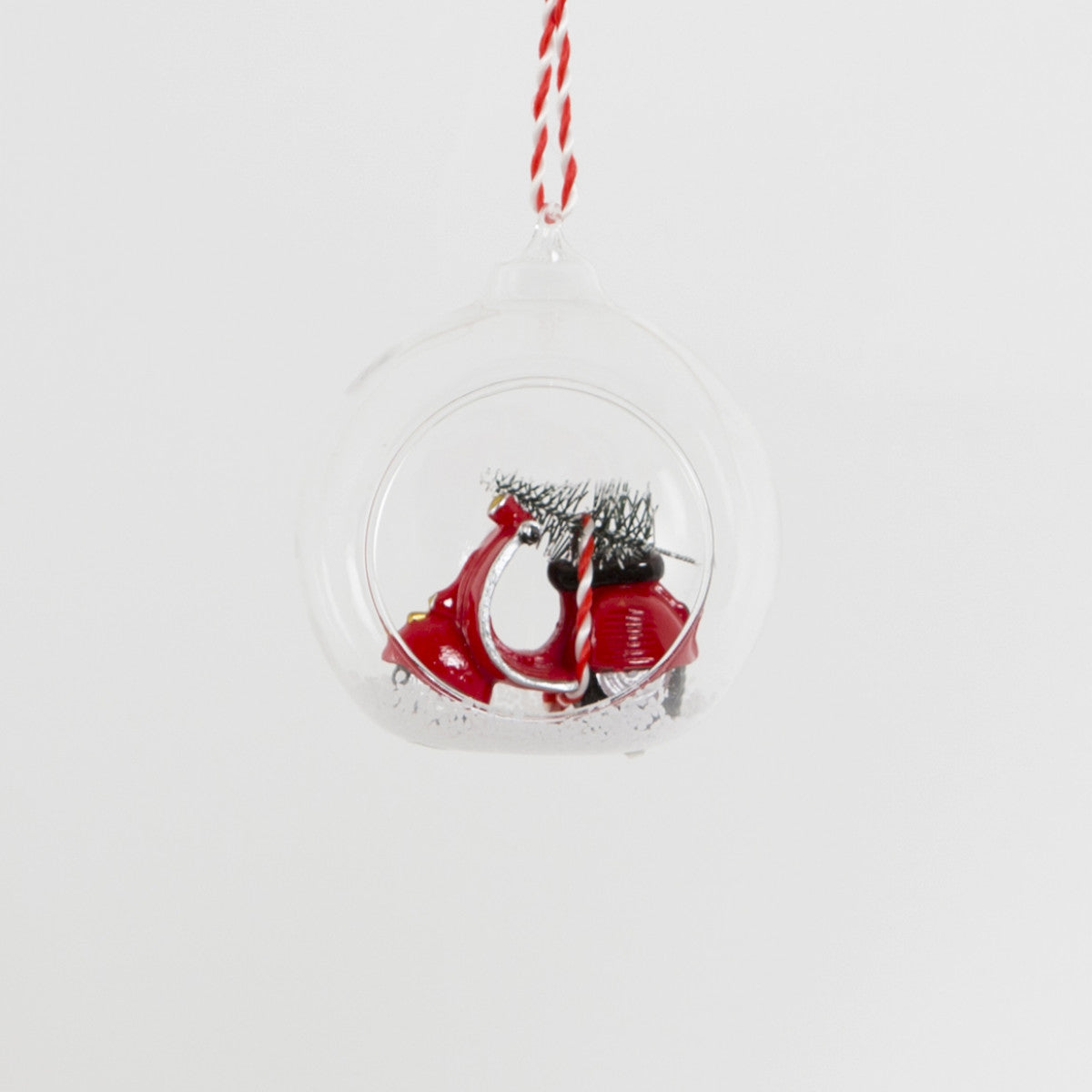 Open glass bauble with a red and white scooter carrying a Christmas tree in the snow.