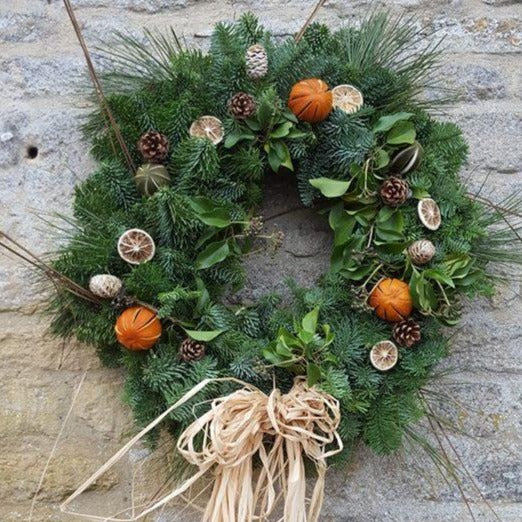 Luxury dried citrus fruits decorate this noble fir Christmas wreath with natural fir cones, completed with a raffia bow.