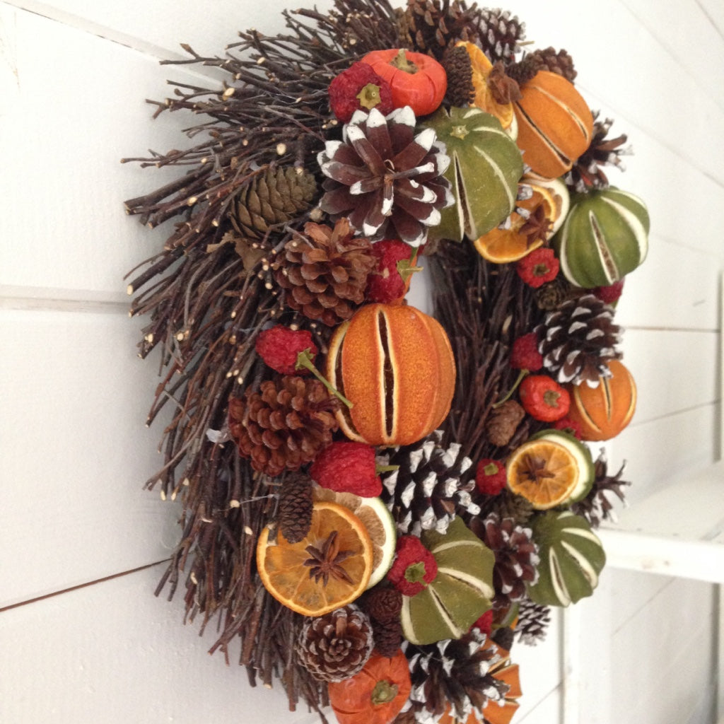 Natural festive green limes oranges, red peppers cones on a natural willow base, creating this Christmas fruit door wreath.