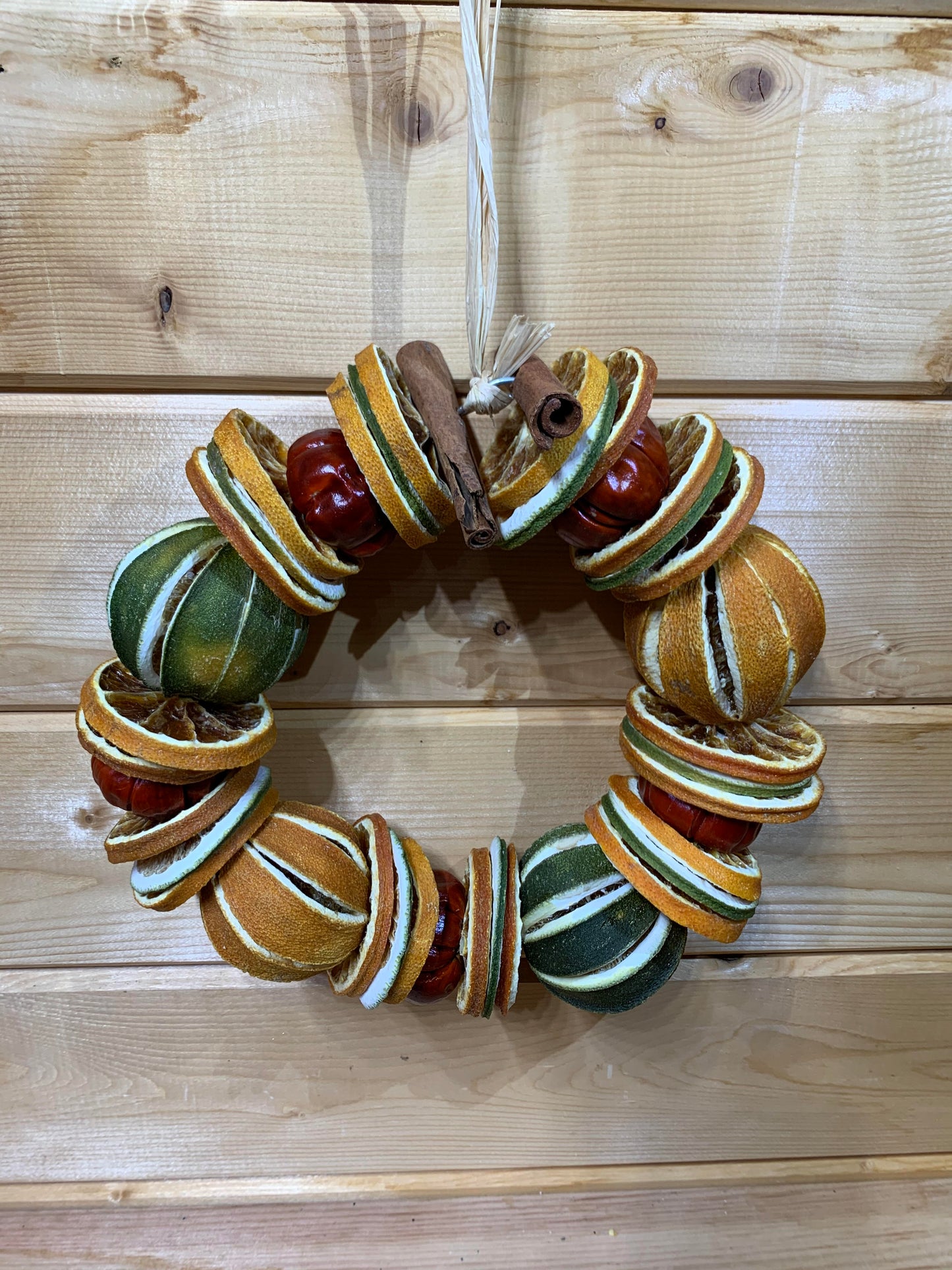 A gorgeous Christmas circle shaped wreath for your door made up of dried whole and sliced oranges and limes, small red peppers and cinnamon sticks on a wire base.